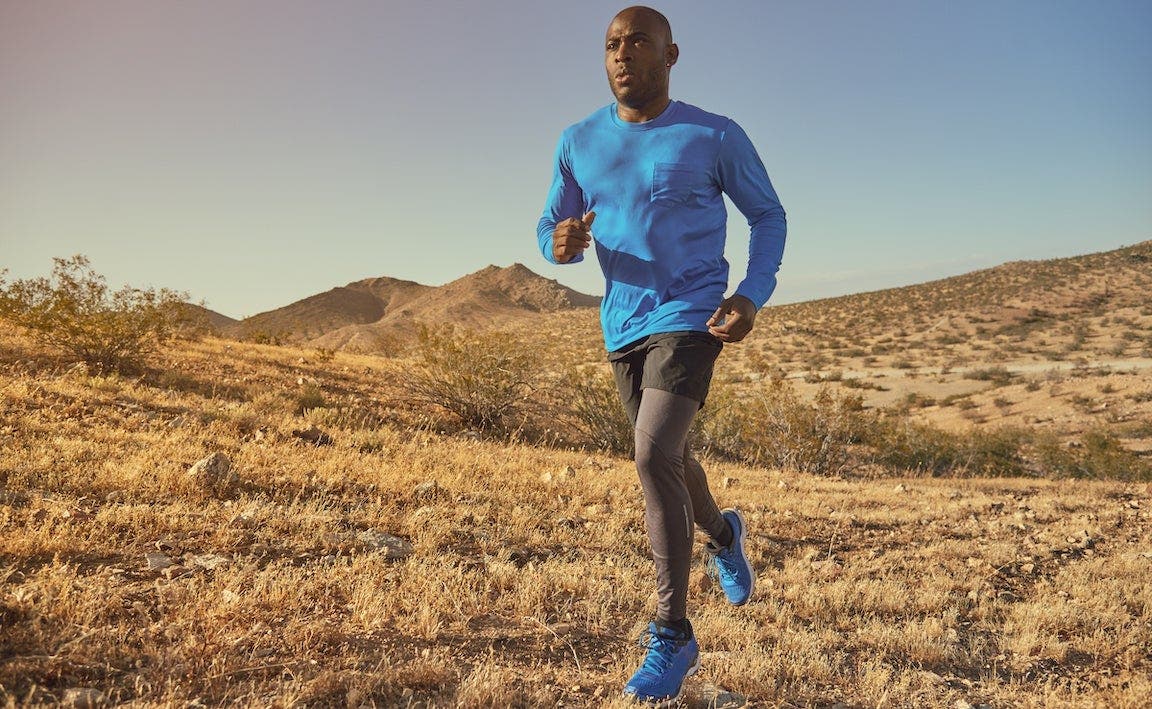 Man in blue running shirt runs across hills.