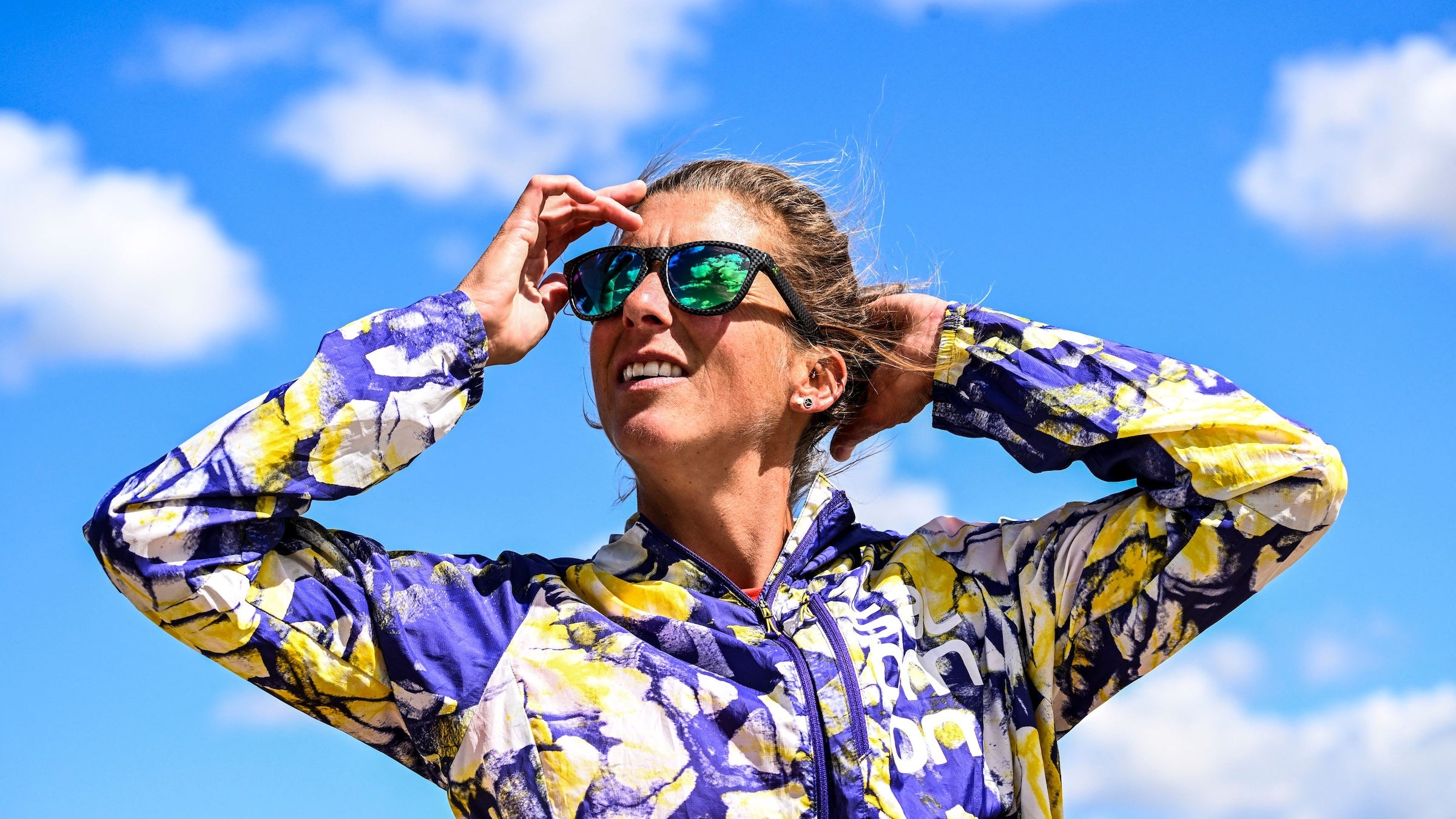 Ultrarunner in a purple and yellow jacket in sunglasses with a blue sky backdrop
