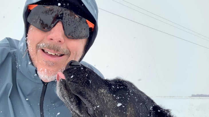 A man runs in the snow with his black dog