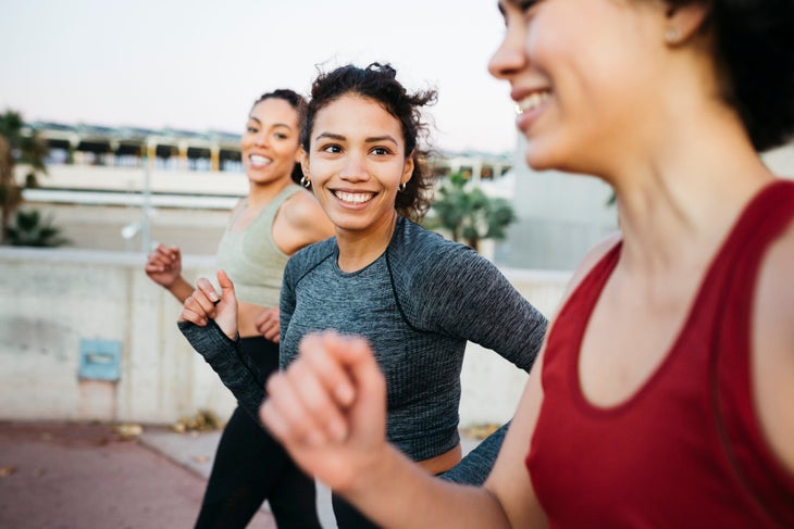 Three smiling young women, wearing sports clothes, jogging on an urban scenario