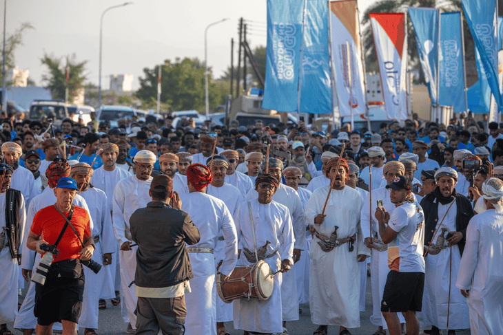 A group of men dressed in formal Omani attire––long-sleeved, ankle-length dishdasha robes, muzzar turbans, and ceremonial curved daggers called a khanjar around the waist—await.