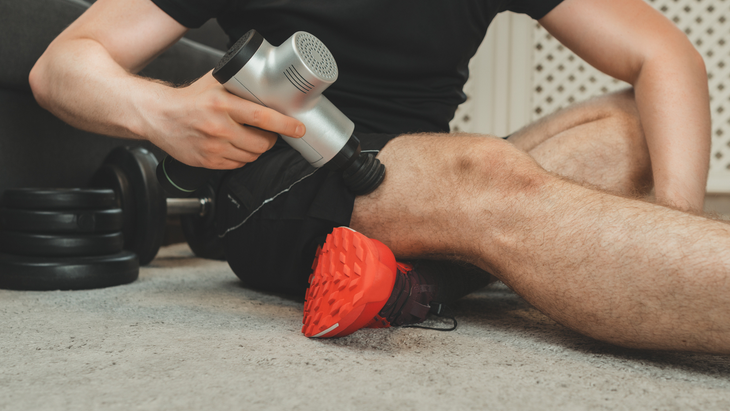 man massaging his quad muscle with a massage gun