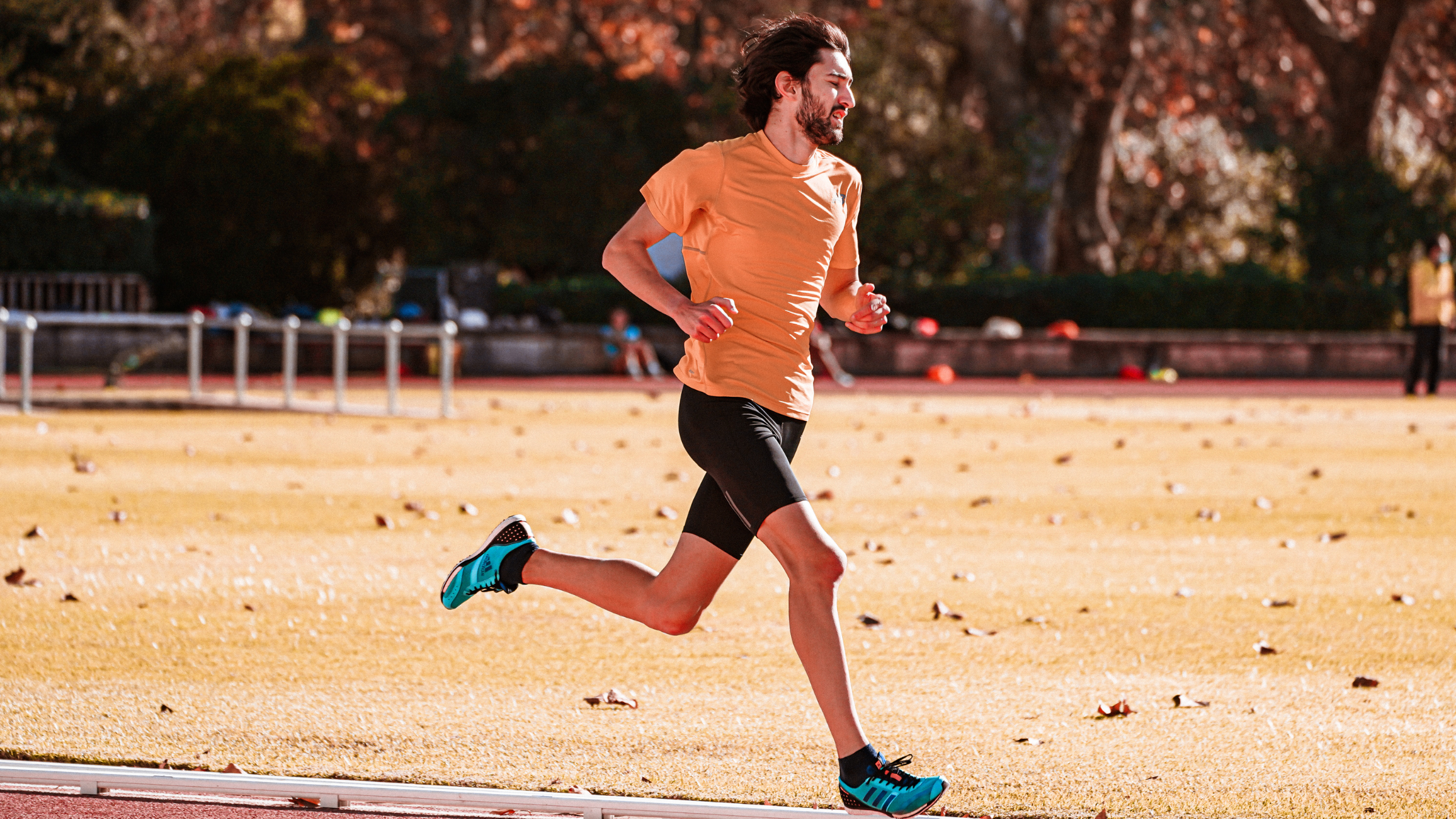 A bearded man in an orange shirt speeds around a track with a pretty good running cadence