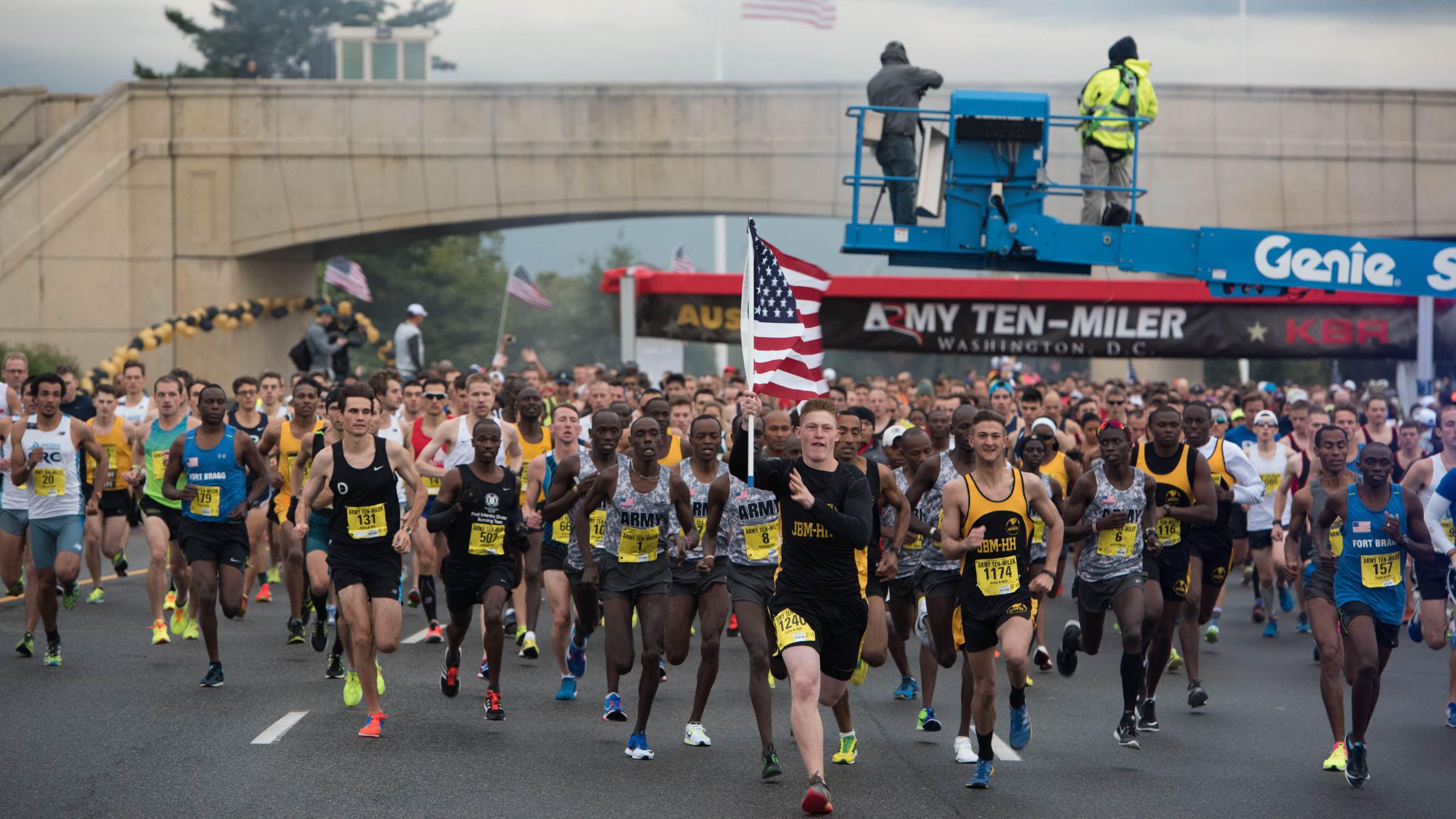 man holding American flag runs at the front of hundreds of runners on road