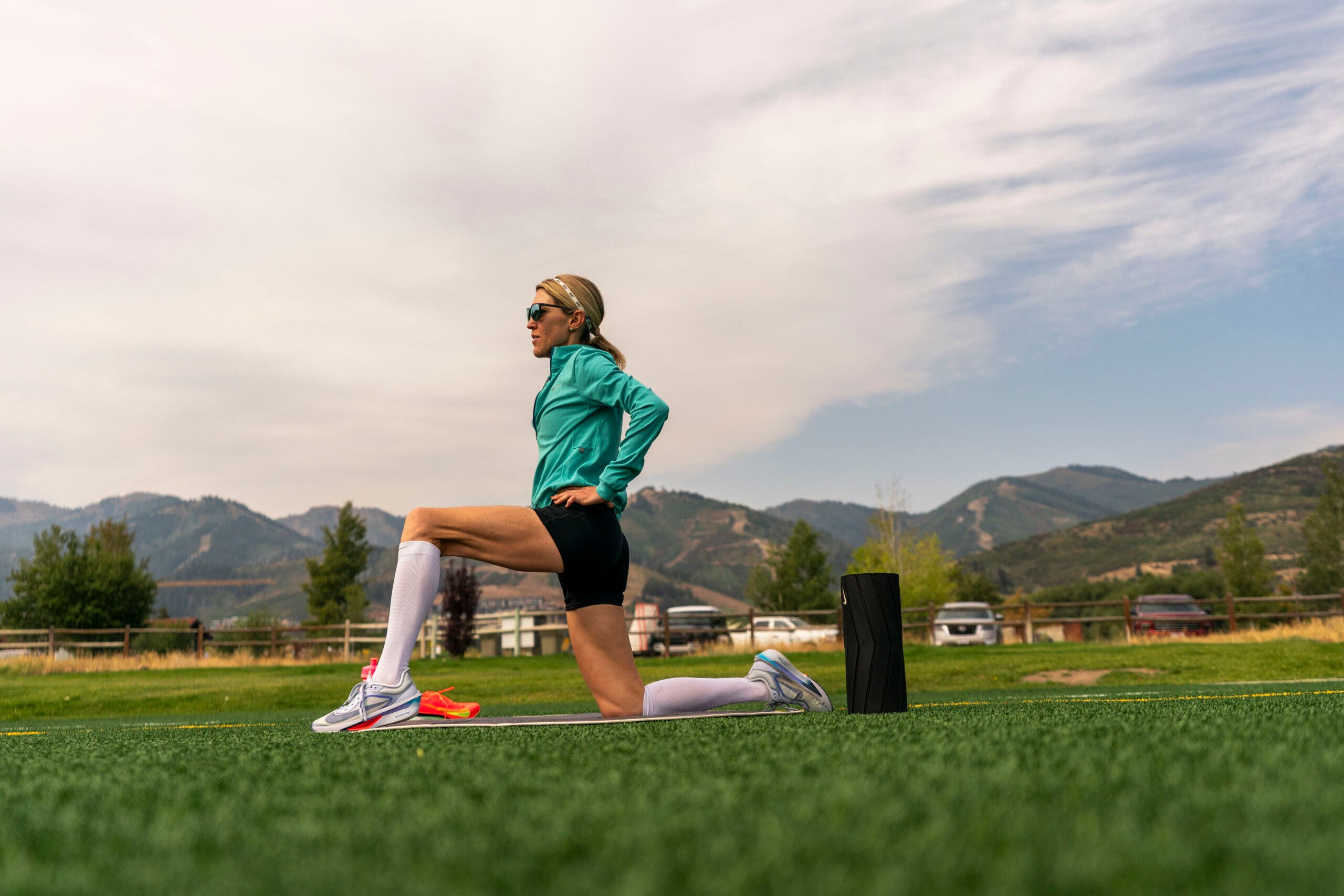 Keira D'Amato does a hip flexor stretch on a grassy field in Park City, Utah.