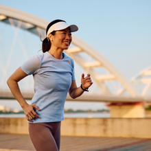 mature Asian woman in running clothes runs with bridge in background, training through menopause