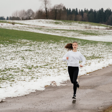 a young woman runs near a field of melting snow