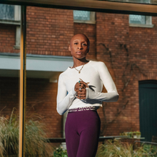 cynthia erivo stands in front of a building. she is wearing running clothing