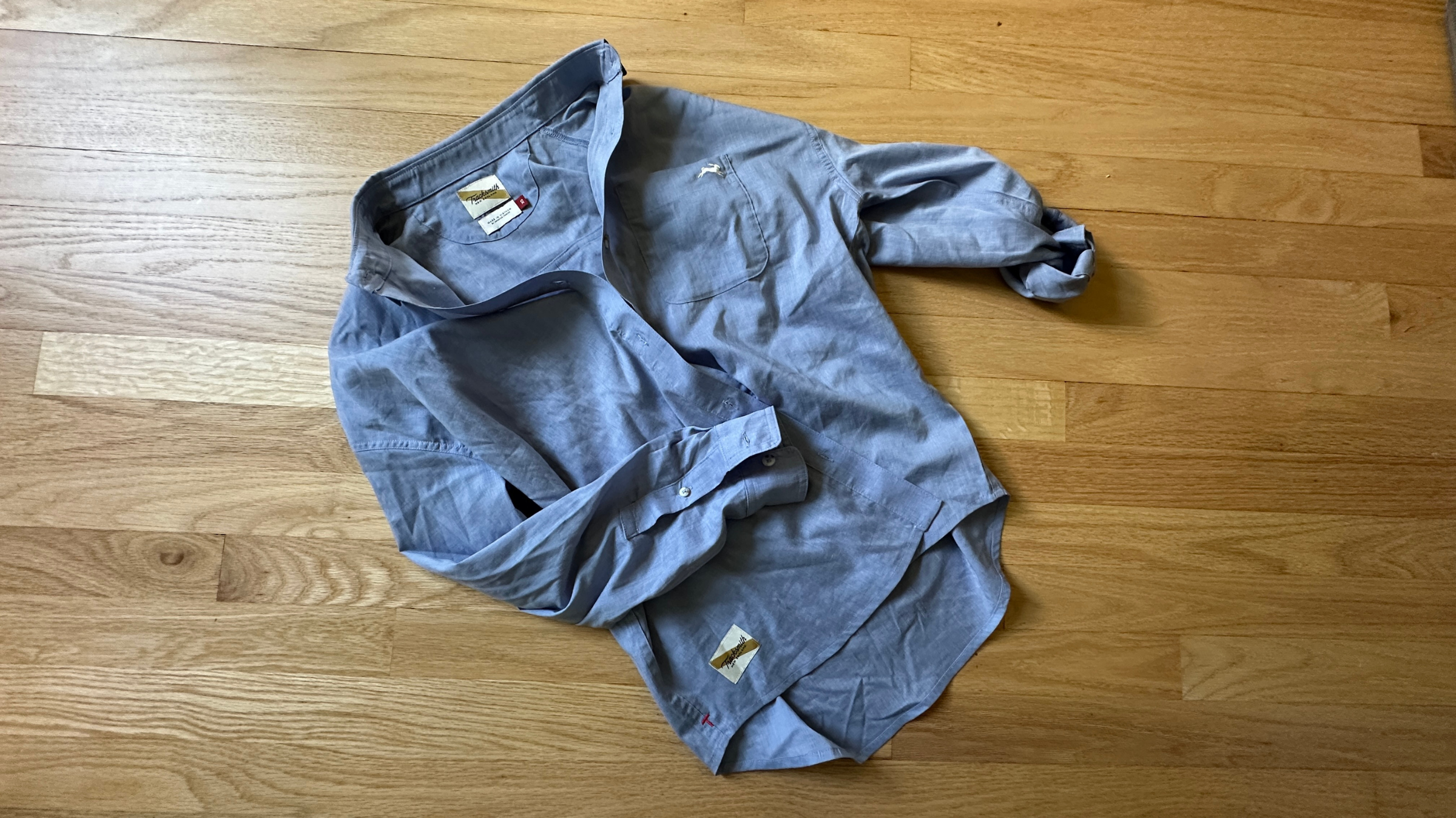 light blue linen button up tracksmith shirt on hardwood floor